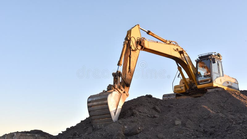 Желтый экскаватор во время earthmoving на открытом карьере на фоне голубого неба.. Строительная техника и earthmoving тяжелое обор стоковая фотография rf
