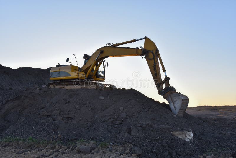 Желтый экскаватор во время earthmoving на открытом карьере на фоне голубого неба.. Строительная техника и earthmoving тяжелое обор стоковое изображение
