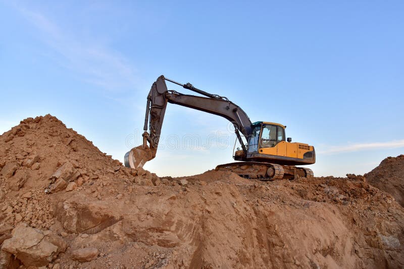 Желтый экскаватор во время earthmoving на открытом карьере на фоне голубого неба.. Строительная техника и earthmoving тяжелое обор стоковая фотография rf