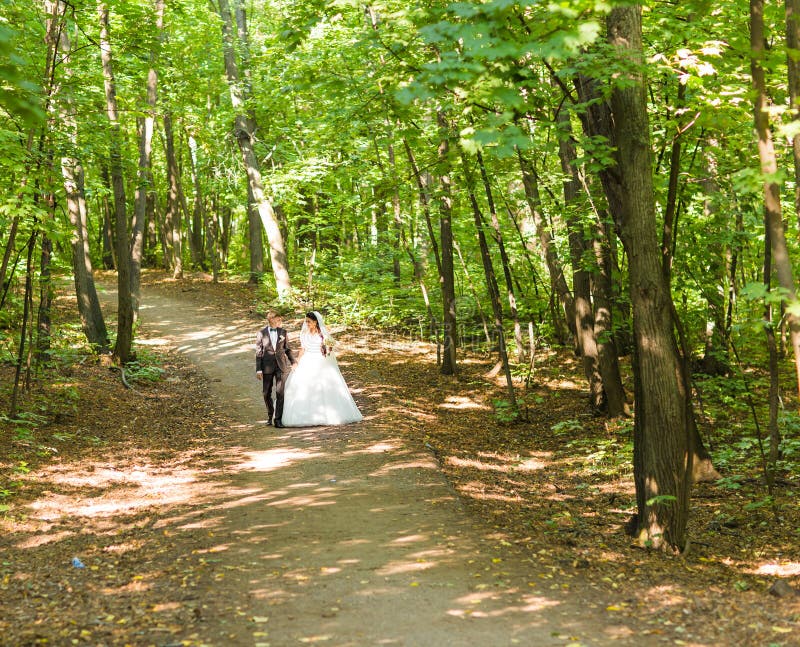 Жених и невеста на дне свадьбы идя Outdoors на природу весны Bridal пары, счастливая женщина новобрачных и обнимать человека стоковая фотография rf Жених и невеста на дне свадьбы идя Outdoors на природу весны Bridal пары, счастливая женщина новобрачных и обнимать человека стоковая фотография rf