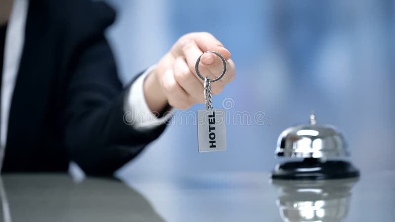 Женская рука держа ключи гостиничного номера около колокола на приеме, обслуживания гостеприимства стоковые изображения rf Женская рука держа ключи гостиничного номера около колокола на приеме, обслуживания гостеприимства стоковые изображения rf