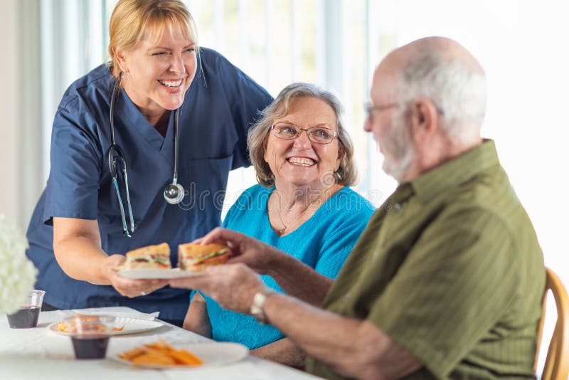 Female Doctor or Nurse Serving Happy Senior Adult Couple Sandwiches at a Senior Assisted Living Home. Female Doctor or Nurse Serving Happy Senior Adult Couple Sandwiches at a Senior Assisted Living Home.