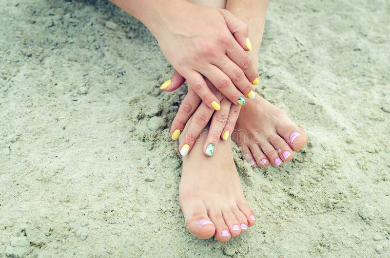 Female hands with manicure and legs with a french pedicure in the sand. Female hands with manicure and legs with a french pedicure in the sand.