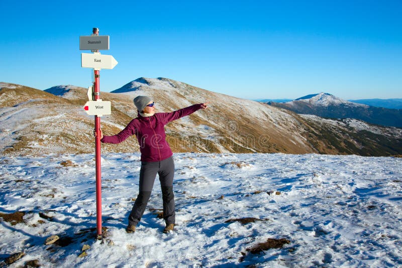 Женский Hiker оставаясь на знаке пути и восхищая сценарный взгляд в горах зимы стоковые фотографии rf Женский Hiker оставаясь на знаке пути и восхищая сценарный взгляд в горах зимы стоковые фотографии rf