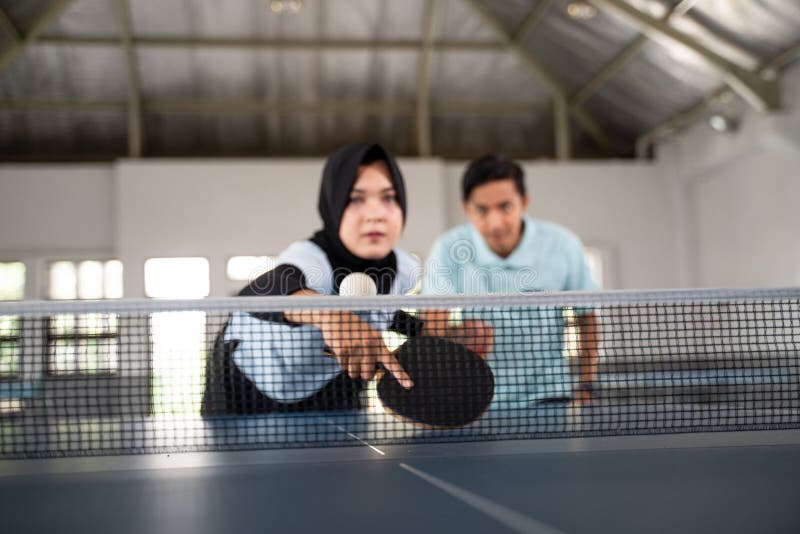 Female ping pong player in hijab hits the ball over the net during double ping pong match. Female ping pong player in hijab hits the ball over the net during double ping pong match