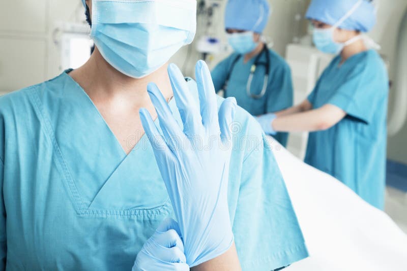 Female surgeon putting on gloves in the operating room, midsection. Female surgeon putting on gloves in the operating room, midsection