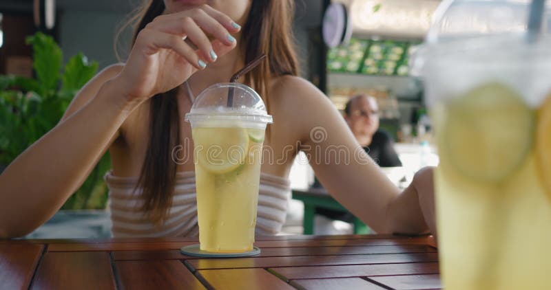 женщина в кафе пьет лимонад ждет заказа в ресторане пьет желтый лимонад через солому использует телефон. деревянный