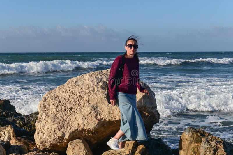 woman in a red jacket against the background of stones and the sea in winter in Cyprus 1. woman in a red jacket against the background of stones and the sea in winter in Cyprus 1