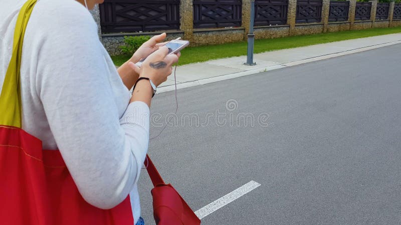 Женщина в наушниках идя на улицу города смотря в смартфоне, применении