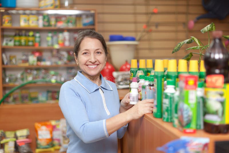 Smiling mature woman chooses agricultural chemicals in the store for gardeners. Smiling mature woman chooses agricultural chemicals in the store for gardeners