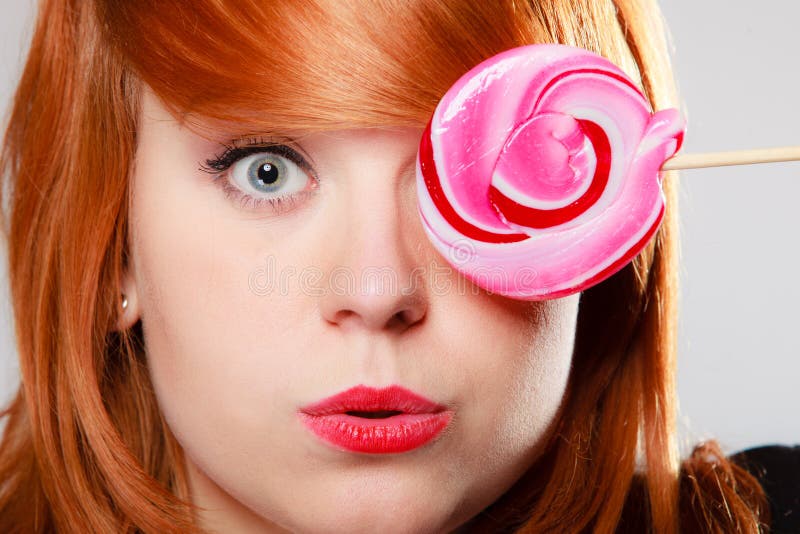 Женщина держа конфету. Девушка Redhair при сладостный леденец на палочке делая потеху стоковое фото Женщина держа конфету. Девушка Redhair при сладостный леденец на палочке делая потеху стоковое фото