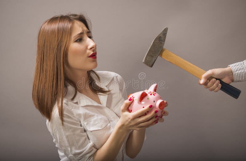 Expressive woman protects their economy piggy bank of someone who is trying to smashing it with a hammer, studio shot on grey background. Expressive woman protects their economy piggy bank of someone who is trying to smashing it with a hammer, studio shot on grey background