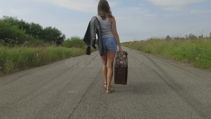 Женщина идет с чемоданом на дороге