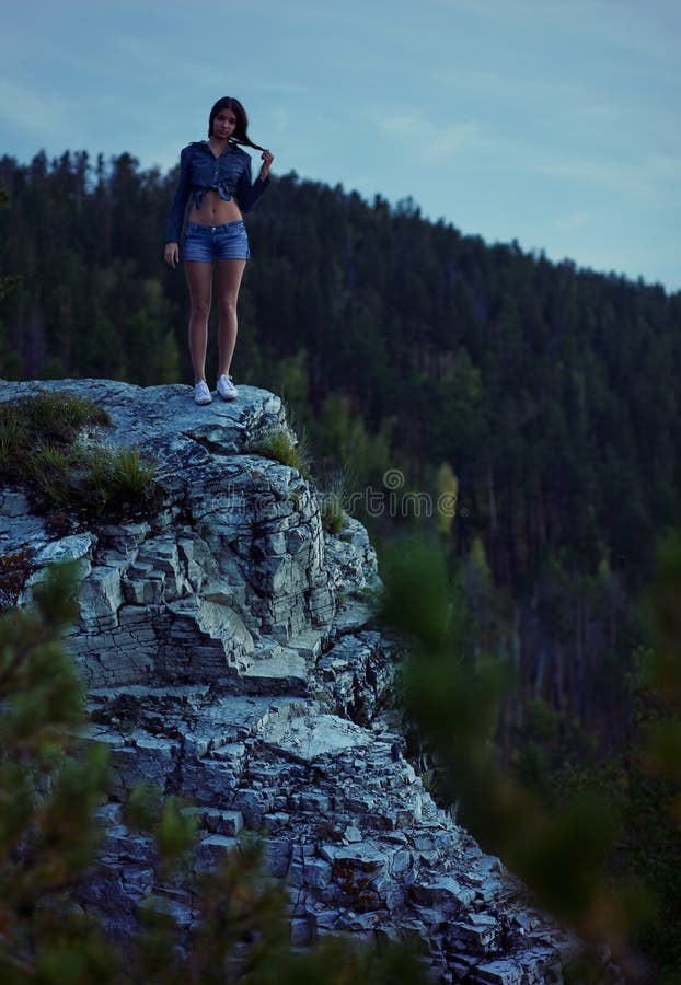 Young woman on edge of cliff with forested mountainside in background. Young woman on edge of cliff with forested mountainside in background.