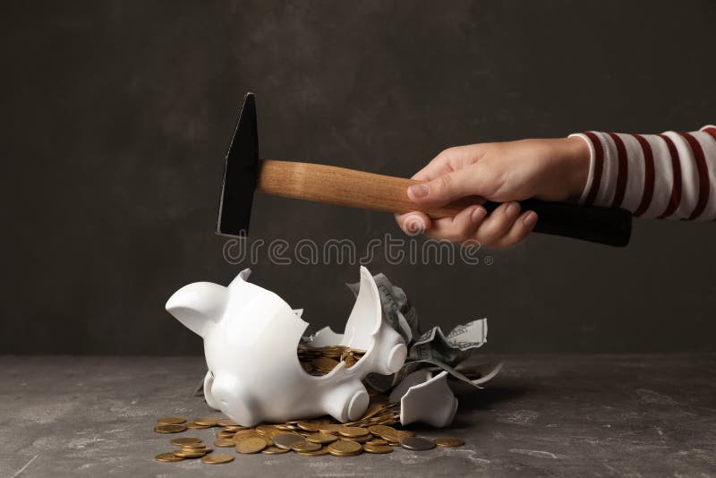 Woman breaking piggy bank with hammer on table. Woman breaking piggy bank with hammer on table