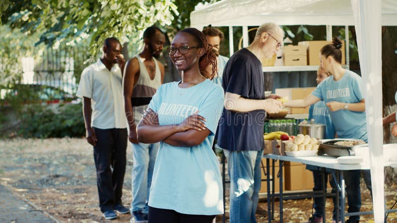 Side-view of black women wearing glasses outside with arms crossed and eyes fixed on camera. Multiethnic volunteers supporting nonprofit initiative aimed at reducing hunger and aiding those in need. Side-view of black women wearing glasses outside with arms crossed and eyes fixed on camera. Multiethnic volunteers supporting nonprofit initiative aimed at reducing hunger and aiding those in need.