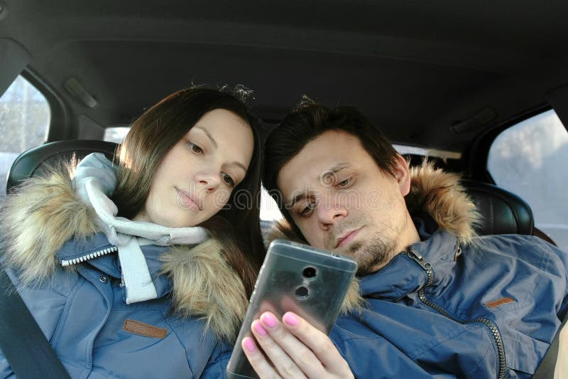 Женщина показывает человеку что-то в мобильном телефоне Они в голубых вниз куртках сидя в автомобиле Вид спереди стоковое изображение rf Женщина показывает человеку что-то в мобильном телефоне Они в голубых вниз куртках сидя в автомобиле Вид спереди стоковое изображение rf