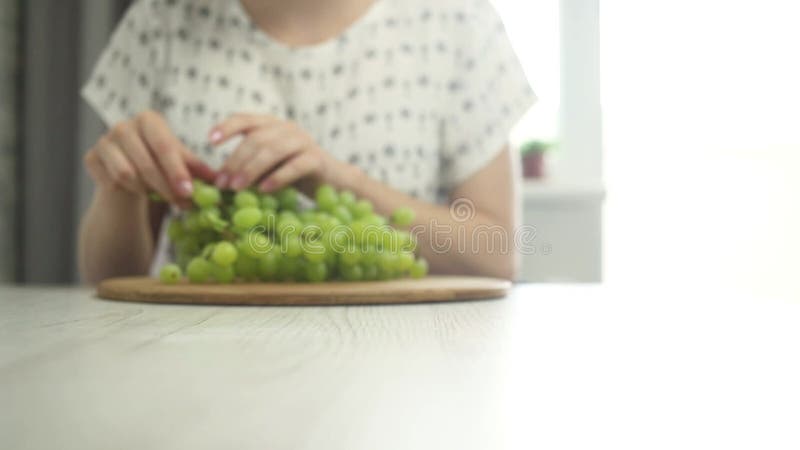 женщина, показывающая деревянную доску с зелёной виноградарью молодая женщина, съедающая виноград