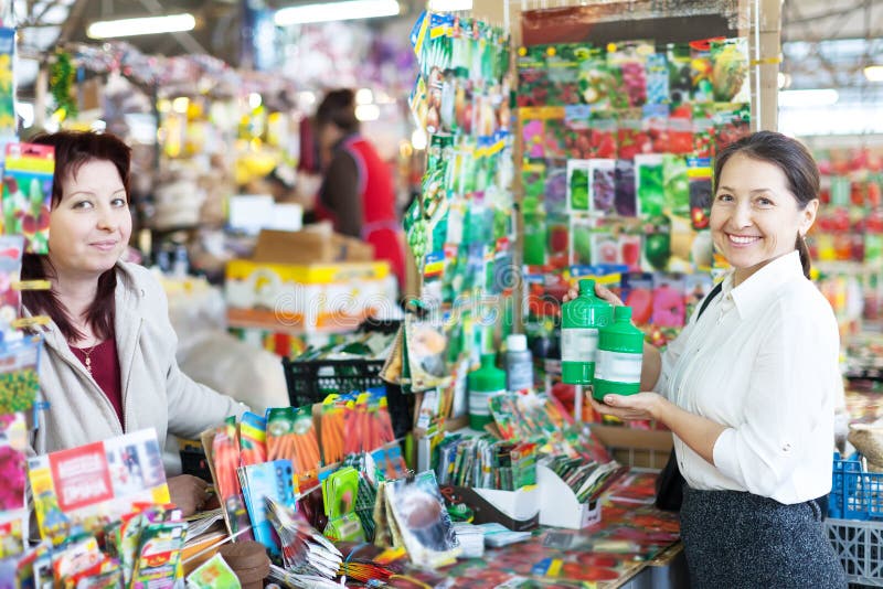 Woman selling liquid fertilizer to mature buyer in store for gardeners. Woman selling liquid fertilizer to mature buyer in store for gardeners