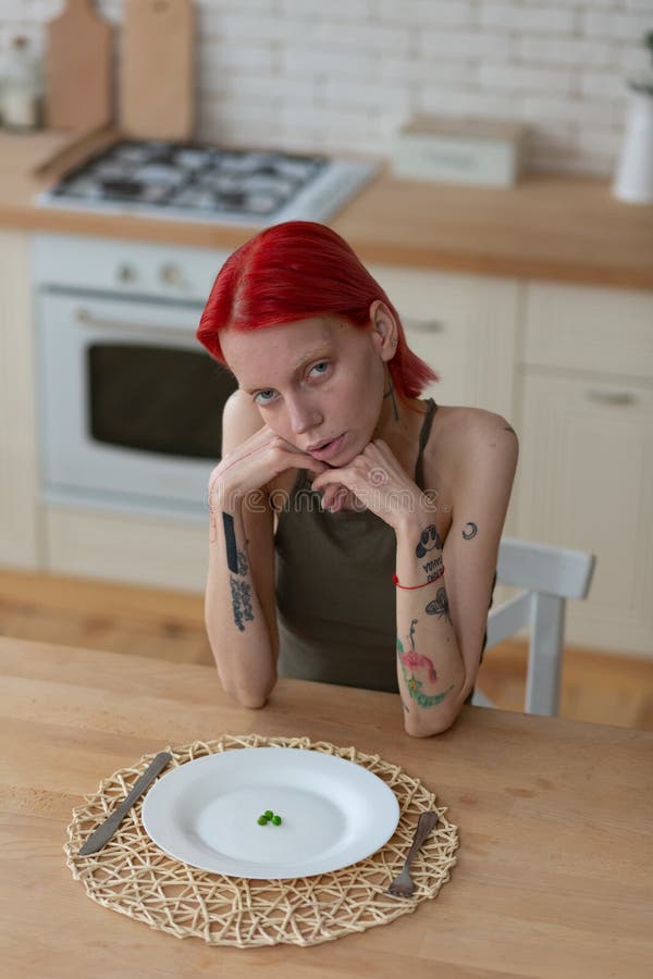 Женщина с анорексией сидя в чувстве кухни плохом стоковая фотография