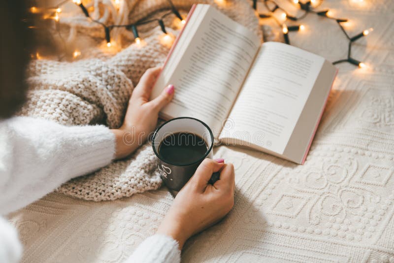 Женщина с уютной чашку холдинга свитер теплых кофе и читать книги стоковое изображение rf