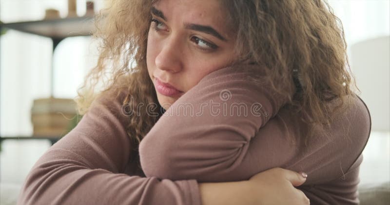Женщина сидит дома с грустным лицом.