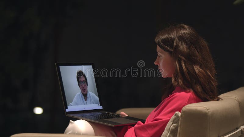 женщина, сидящая на диване с видеоконференц-залом с мужчиной на экране