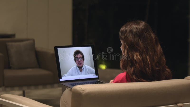 женщина, сидящая на диване с видеоконференц-залом с мужчиной на экране