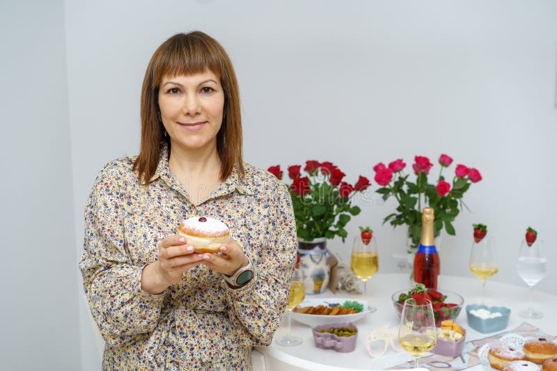 женщина средних лет наслаждается суфганией среди праздничного стола хануки. стоковые фото