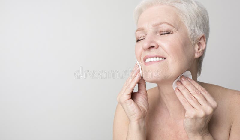 Attractive senior woman enjoying her beauty and face care routine, cleansing skin with cotton pads. Panorama with copy space. Attractive senior woman enjoying her beauty and face care routine, cleansing skin with cotton pads. Panorama with copy space