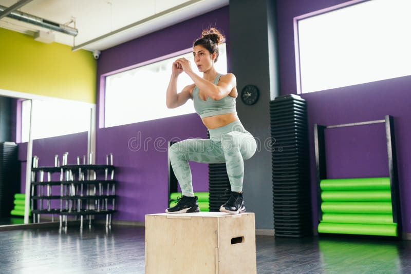 Fitness woman jumping onto a box as part of exercise routine. Caucasian female doing box jump workout at gym. Fitness woman jumping onto a box as part of exercise routine. Caucasian female doing box jump workout at gym.