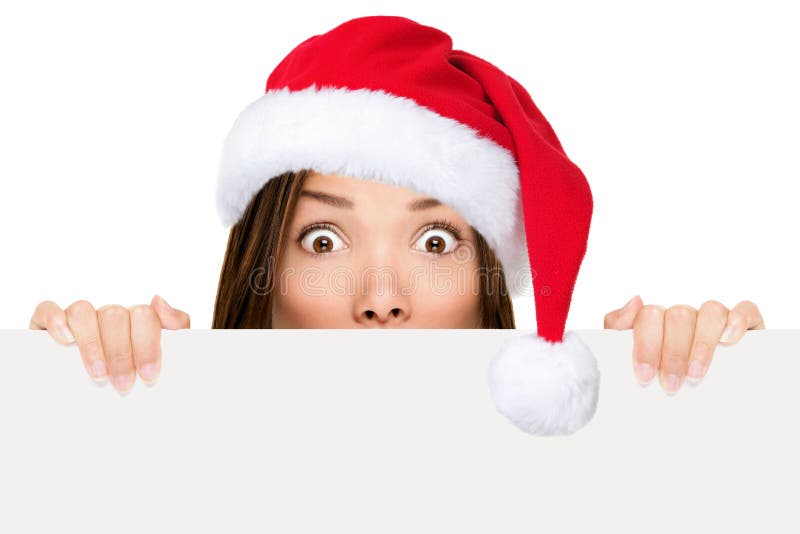 Santa hat woman showing christmas sign peeking over edge wearing red santa hat with funny expression. Mixed race asian chinese / caucasian woman portrait isolated on white background. Santa hat woman showing christmas sign peeking over edge wearing red santa hat with funny expression. Mixed race asian chinese / caucasian woman portrait isolated on white background.