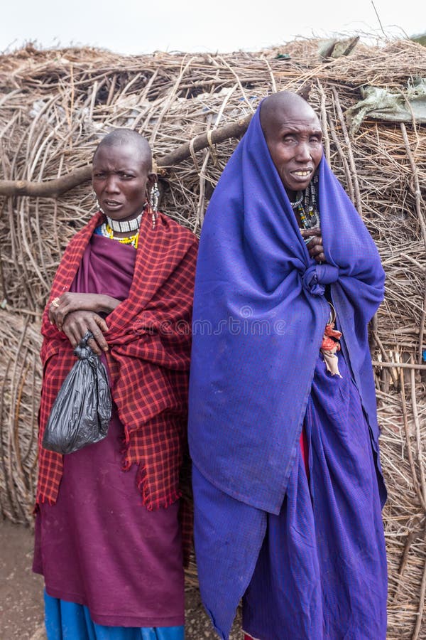 2 женщины Maasai стоят около их взгляда дома на моей камере с интересовать стоковые фотографии rf 2 женщины Maasai стоят около их взгляда дома на моей камере с интересовать стоковые фотографии rf