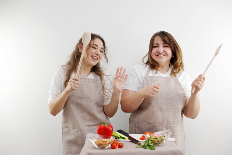 2 women dancing while preparing tasty and healthy food vegetarian food vegetable salad in hands wooden spoons identical kitchen aprons. 2 women dancing while preparing tasty and healthy food vegetarian food vegetable salad in hands wooden spoons identical kitchen aprons