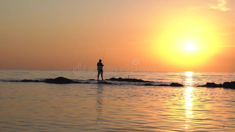 Живописный вид на закат в океане с силуэтом человека ловить рыбу.