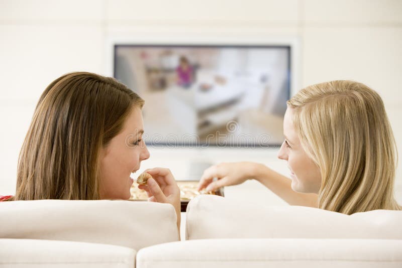Two women in living room watching television eating. Two women in living room watching television eating
