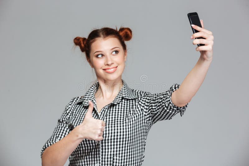 Жизнерадостная женщина показывая большие пальцы руки вверх и принимая selfie с smartphone стоковая фотография Жизнерадостная женщина показывая большие пальцы руки вверх и принимая selfie с smartphone стоковая фотография