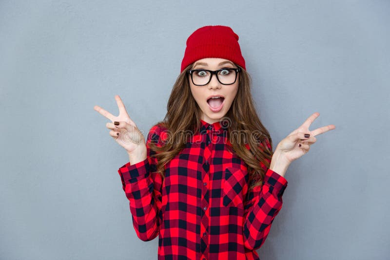 Portrait of a cheerful trendy woman showing two fingers sign over gray background. Portrait of a cheerful trendy woman showing two fingers sign over gray background