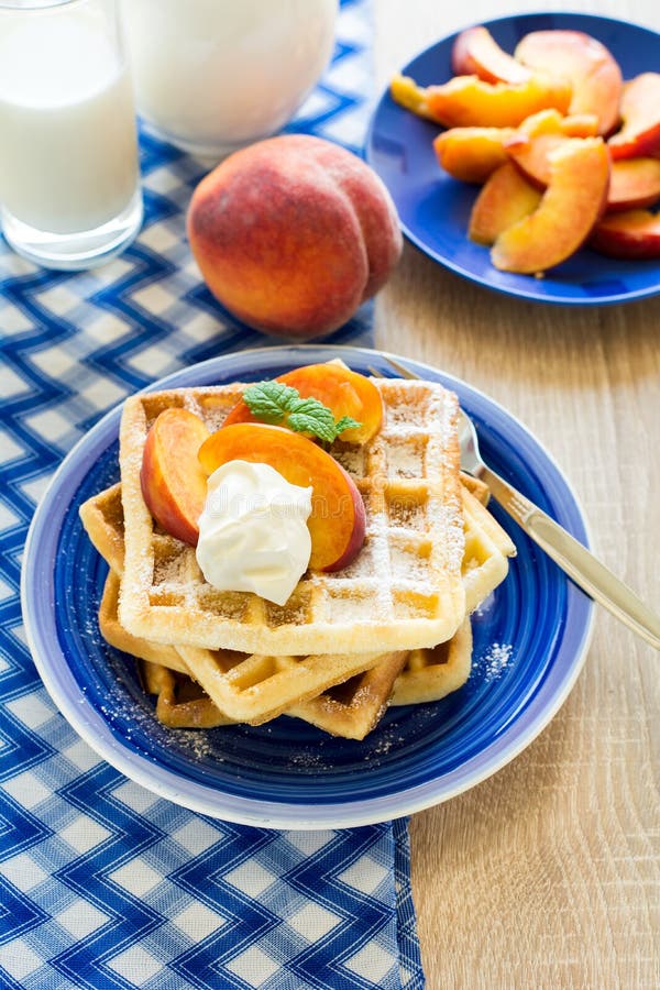Здоровый завтрак: Бельгийские waffles с кусками персика и сливк украсили листья мяты и голубую салфетку стоковое изображение Здоровый завтрак: Бельгийские waffles с кусками персика и сливк украсили листья мяты и голубую салфетку стоковое изображение