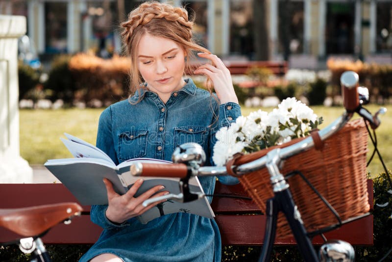 Заботливая книга readng женщины и мечтать на beanch outdoors стоковое изображение rf Заботливая книга readng женщины и мечтать на beanch outdoors стоковое изображение rf
