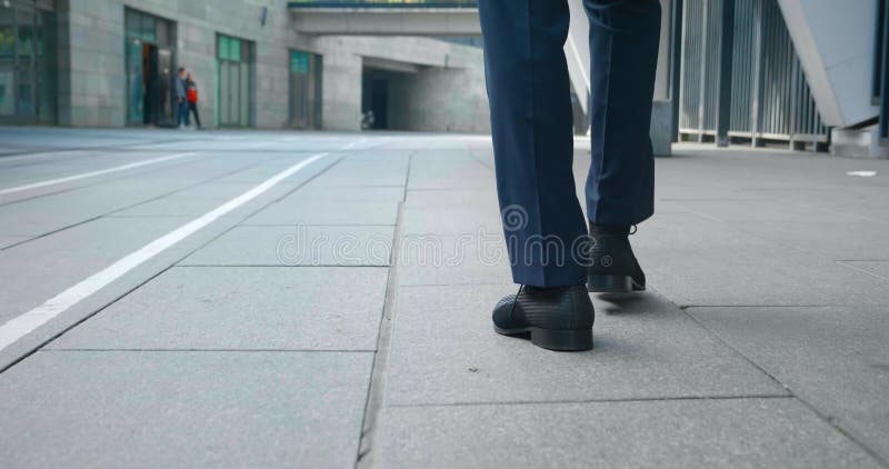 задний вид уверенного человека в кожаных туфлях и формальном костюме, идущем по городу рядом с офисным зданием. ступни заднего вид