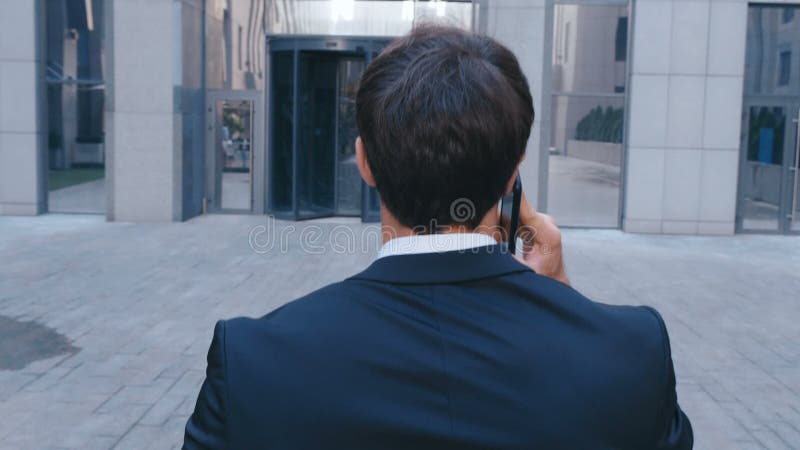 Задний обзор уверенный бизнесмен разговаривает по телефону и ходит по улице в офисе Концепция: технология