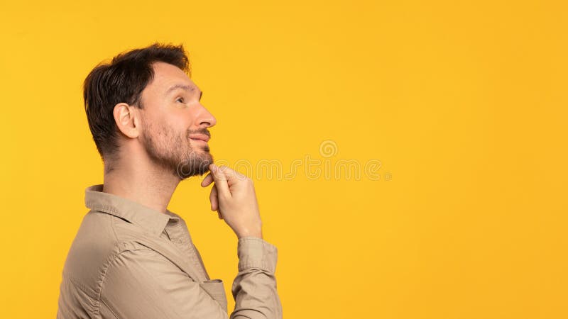 A man is captured in profile as he looks thoughtfully upwards, gently resting his chin on his hand, set against a bright yellow backdrop that accentuates the contemplative mood, copy space. A man is captured in profile as he looks thoughtfully upwards, gently resting his chin on his hand, set against a bright yellow backdrop that accentuates the contemplative mood, copy space