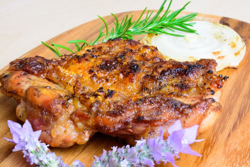 BBQ grilled boneless chicken thigh with an onion slice and with rosemary and lavender garnish on a neutral background and served on a wooden plank. BBQ grilled boneless chicken thigh with an onion slice and with rosemary and lavender garnish on a neutral background and served on a wooden plank