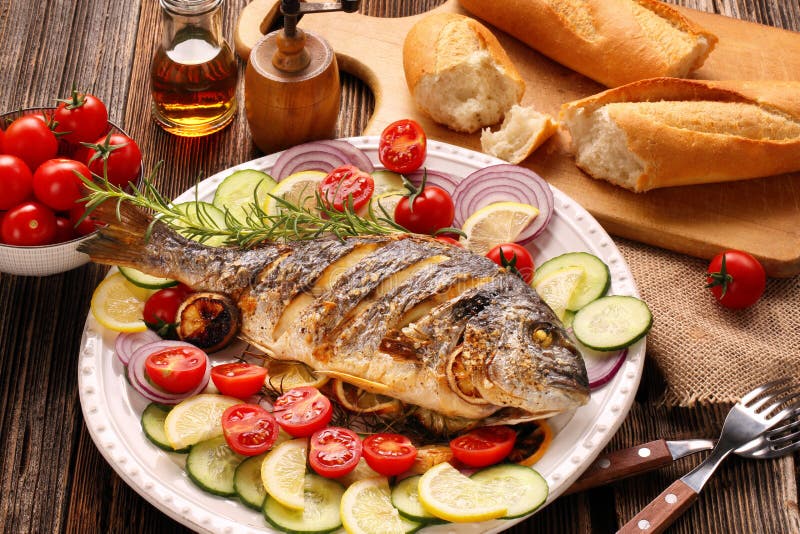 Зажаренные в духовке рыбы dorada с овощами на деревянной предпосылке стоковое изображение Зажаренные в духовке рыбы dorada с овощами на деревянной предпосылке стоковое изображение