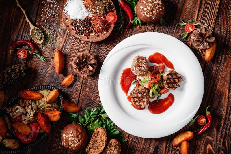 Зажаренные медальоны мяса с испаренными овощами и красным соусом на белой плите стоковые изображения rf Зажаренные медальоны мяса с испаренными овощами и красным соусом на белой плите стоковые изображения rf