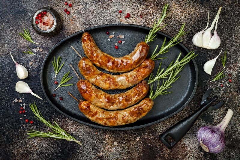 Grilled homemade rosemary sausages skewers on iron frying pan over rustic dark stone kitchen table. Top view, flat lay. Grilled homemade rosemary sausages skewers on iron frying pan over rustic dark stone kitchen table. Top view, flat lay