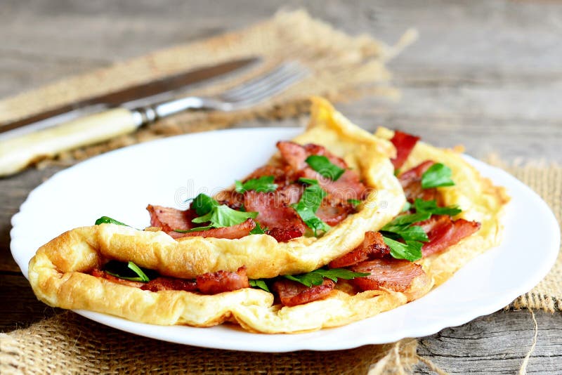 Зажаренный заполненный омлет Домодельный вкусный омлет с беконом и петрушкой на плите, вилкой, ножом на старой деревянной предпос стоковые фото Зажаренный заполненный омлет Домодельный вкусный омлет с беконом и петрушкой на плите, вилкой, ножом на старой деревянной предпос стоковые фото