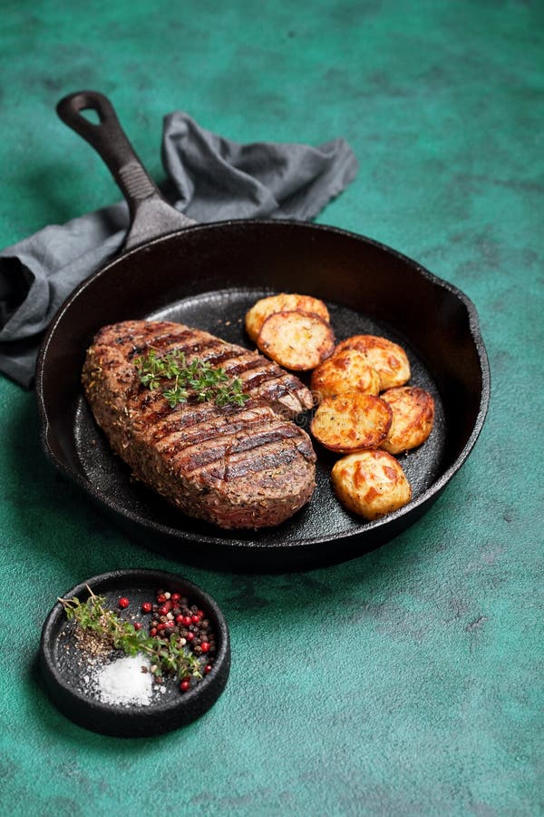 Зажаренный стейк говядины и испеченная картошка в skillet литого железа стоковые фотографии rf Зажаренный стейк говядины и испеченная картошка в skillet литого железа стоковые фотографии rf