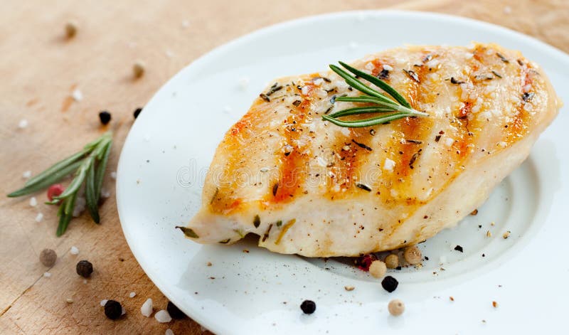 Grilled chicken breast with rosemary on white plate with wooden background - trendy rustic composition. Grilled chicken breast with rosemary on white plate with wooden background - trendy rustic composition